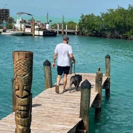 A person walking a dog along a dock beside turquoise water.